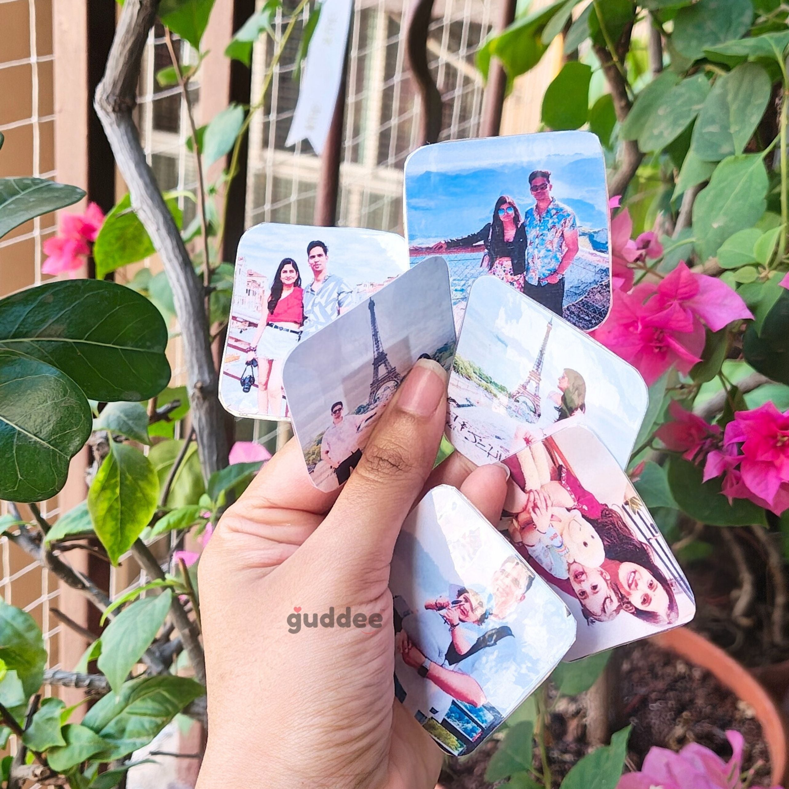 A hand arranging multiple custom square photo magnets on a kitchen fridge to create a memory collage.