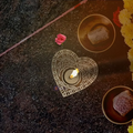 An illuminated handcrafted Sheesham wood heart mandala candle holder diffusing a warm amber flame on a cozy bedroom table.