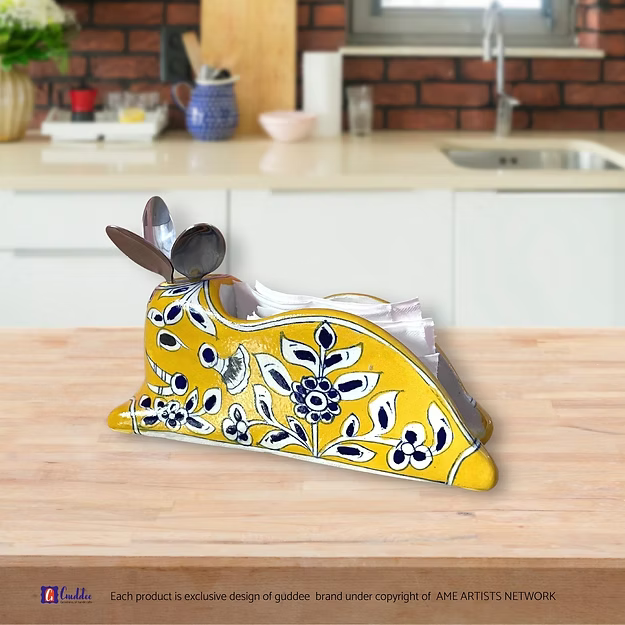 A handcrafted yellow royale blue pottery caddy holding folded tissues and silverware neatly on a modern wooden dining table.