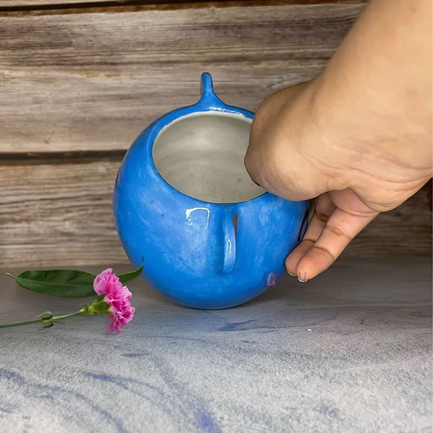 Hand holding a blue ceramic pot with a wooden background