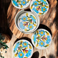 Five round white ceramic blue pottery coasters fanned out on a wooden coffee table showing traditional hand-painted motifs.