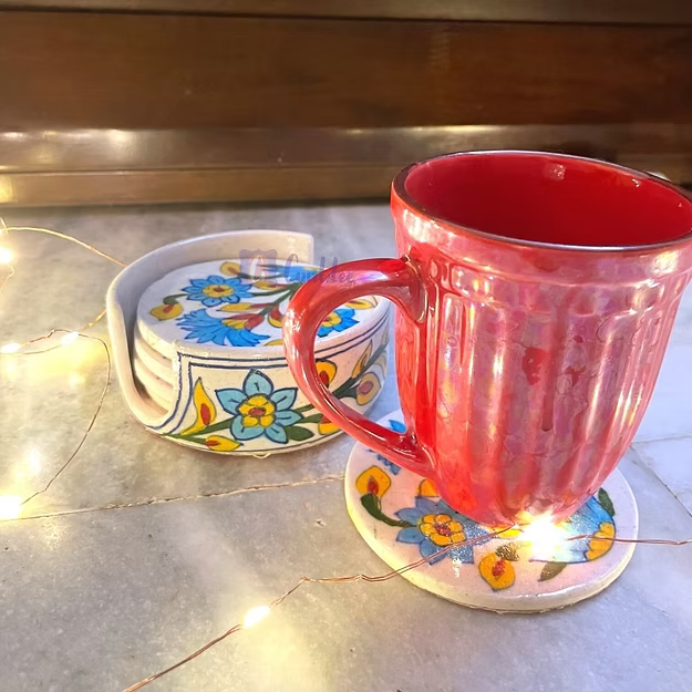 Red mug on a floral coaster with string lights on a counter