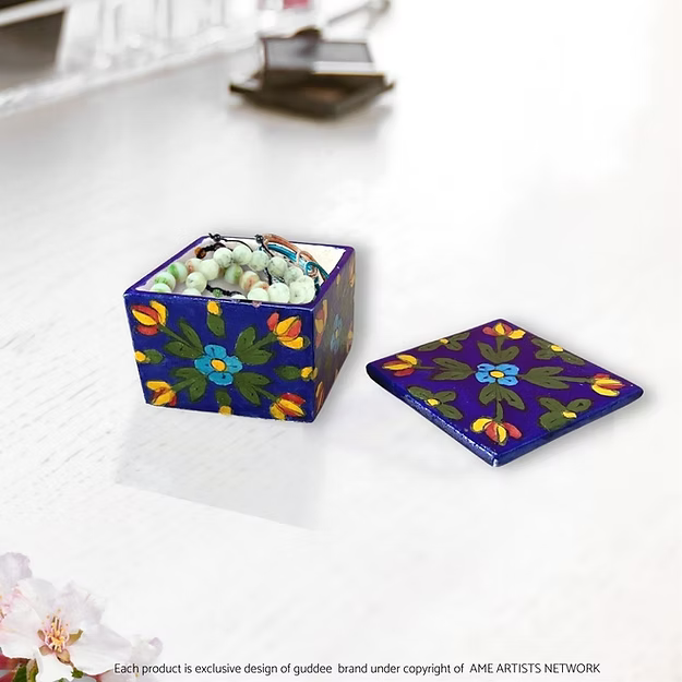 A handcrafted mini floral blossom blue pottery box opened on a vanity table to show rings and small jewelry stored safely inside.