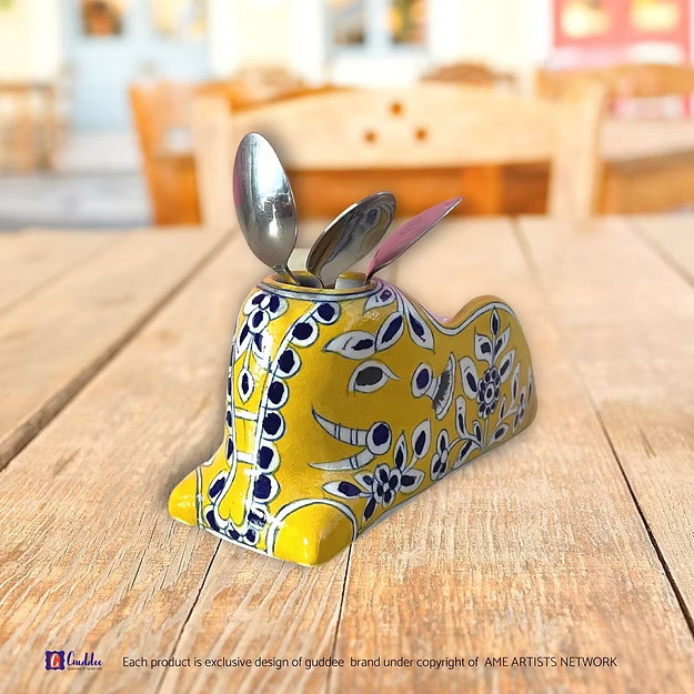 A handcrafted yellow royale blue pottery caddy holding folded tissues and silverware neatly on a modern wooden dining table.