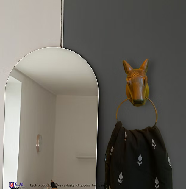 A handcrafted rustic wooden horse wall hanger rack holding a coat and keys near a warm contemporary home entry door.