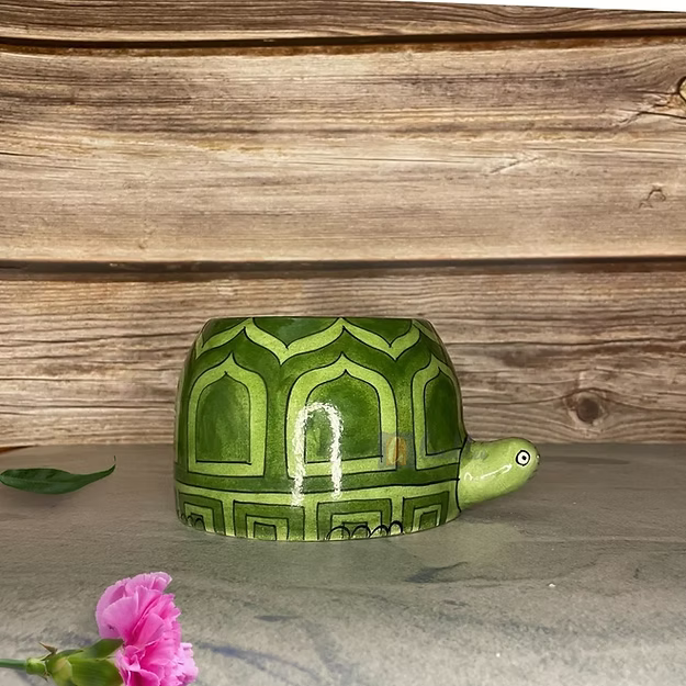 A vibrant green succulent plant growing inside Guddee's handcrafted ceramic green pottery tortoise animal planter on a bright desk.
