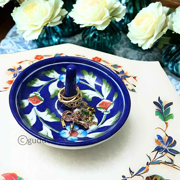 Gold engagement rings and jewelry stored elegantly inside a dark blue handcrafted ceramic blue pottery trinket dish.