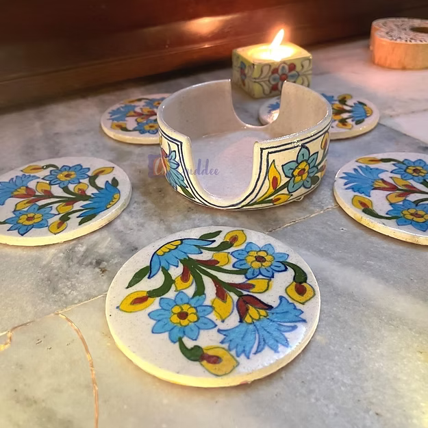Five round white ceramic blue pottery coasters fanned out on a wooden coffee table showing traditional hand-painted motifs.