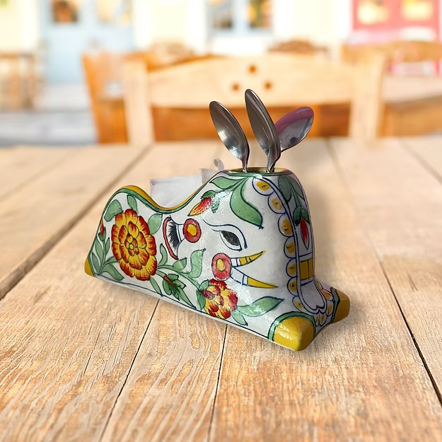 A handcrafted marigold blue pottery caddy holding folded tissues and silverware neatly on a modern wooden dining table.