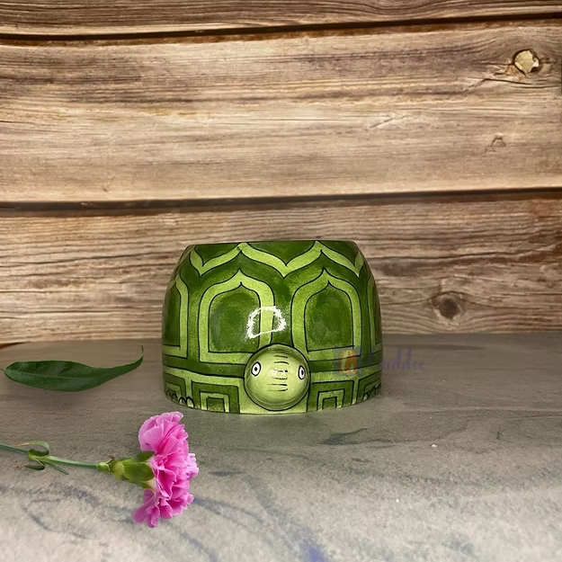 A vibrant green succulent plant growing inside Guddee's handcrafted ceramic green pottery tortoise animal planter on a bright desk.