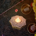 A lit rosewood mandala tea light holder sitting as a warm decorative centerpiece table runner accent on a wooden table.
