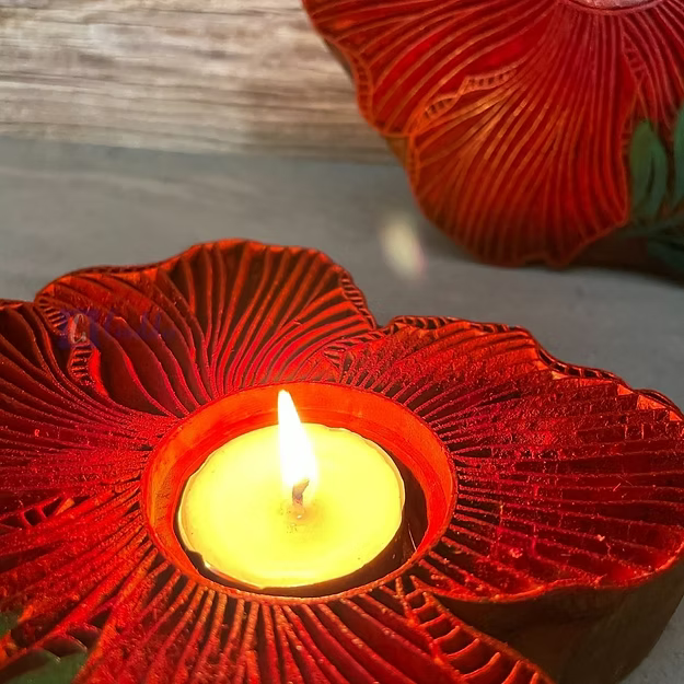 A lit rosewood hibiscus tea light holder sitting as a warm decorative centerpiece table runner accent on a wooden dining table.