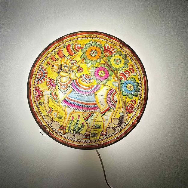 A lit synthetic leather Nandi cow silhouette electric bulb lamp casting a powerful devotional shadow profile across a pooja room wall.