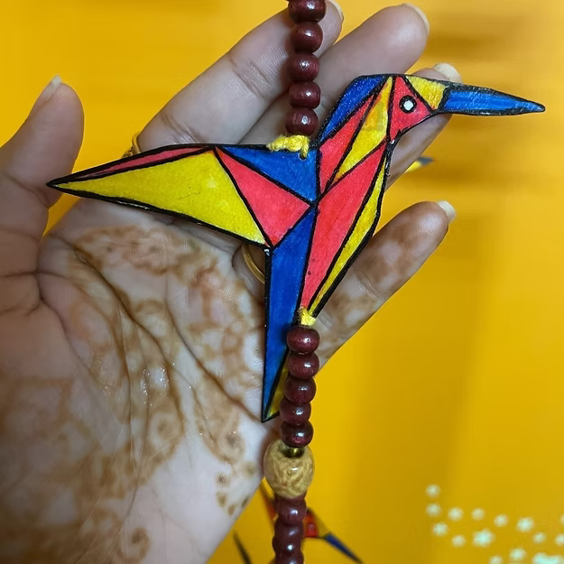 Colorful geometric bird ornament held by a hand against a yellow background