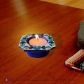 A glowing candle inside a dark blue handcrafted ceramic floral mini tea light holder creating ambient lighting on a tabletop.