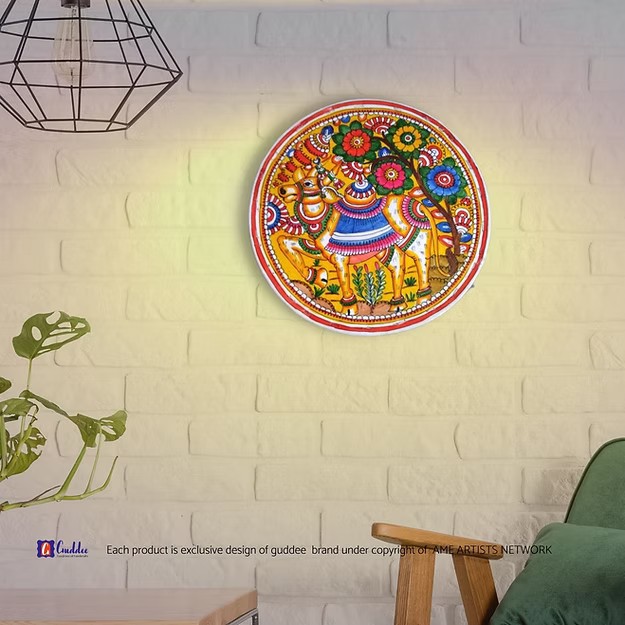 A lit translucent Tholu Bommalata leather Nandi sconce projecting a glowing, multi-colored folk pattern on a hallway wall.