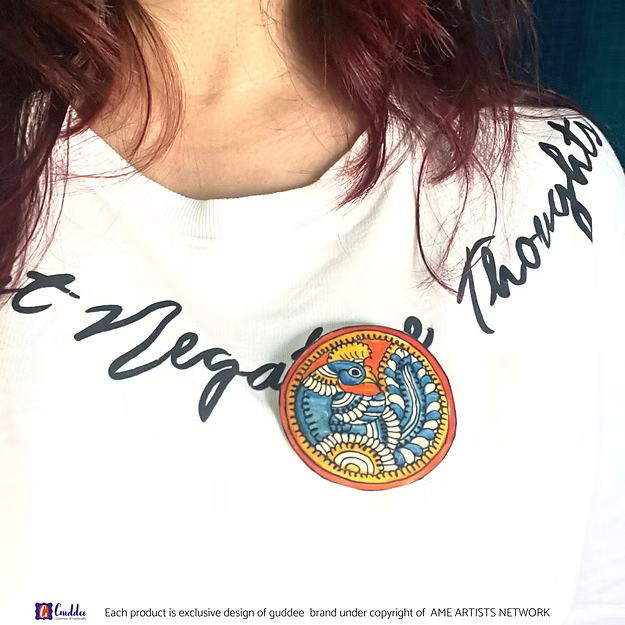 A handcrafted Tholu Bommalata Blue Peacock leather brooch pinned elegantly as a wearable art fashion statement on clothing.