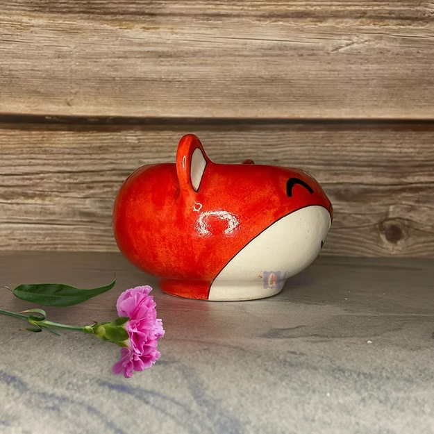 Red and white ceramic fox-shaped container with a pink flower on a wooden surface