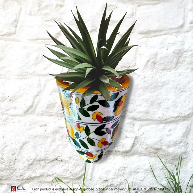 A handcrafted Masti yellow blue pottery wall pocket pot holding fresh green herbs on a modern apartment balcony wall.