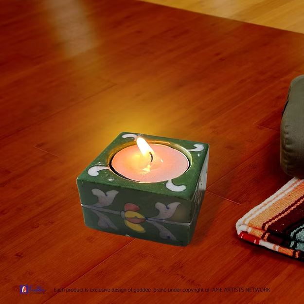 A lit ceramic dark green square candle holder casting a warm ambient glow as a decorative coffee table centerpiece accent.