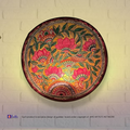 A lit translucent Tholu Bommalata leather Lotus sconce projecting a glowing, multi-colored folk pattern on a hallway wall.