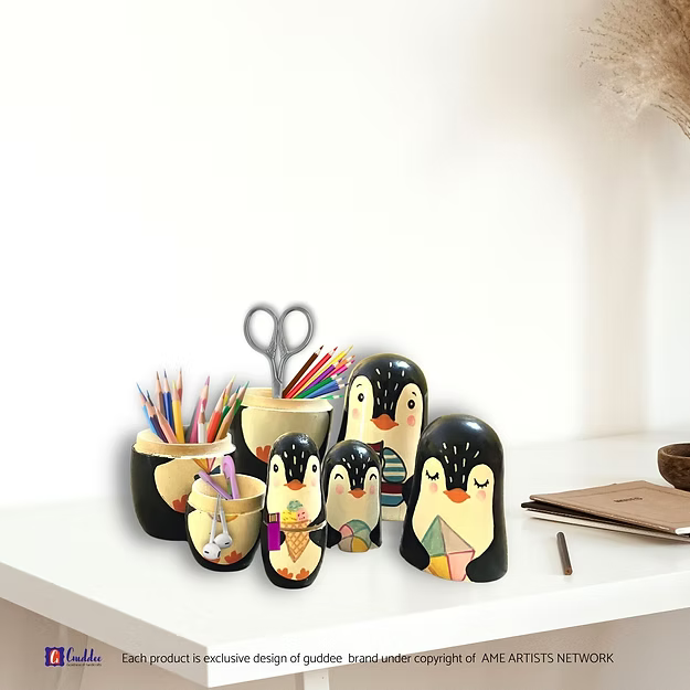 Handcrafted penguin nesting boxes opened on a desk to reveal house keys, coins, and AirPods stored safely inside.