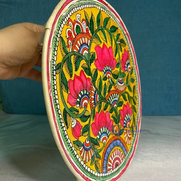 Decorative plate with floral patterns held by a hand against a blue background